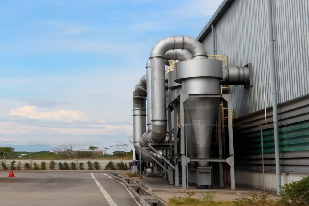 Air pollution control: dust cyclone collection and chimney stack outside industrial building.